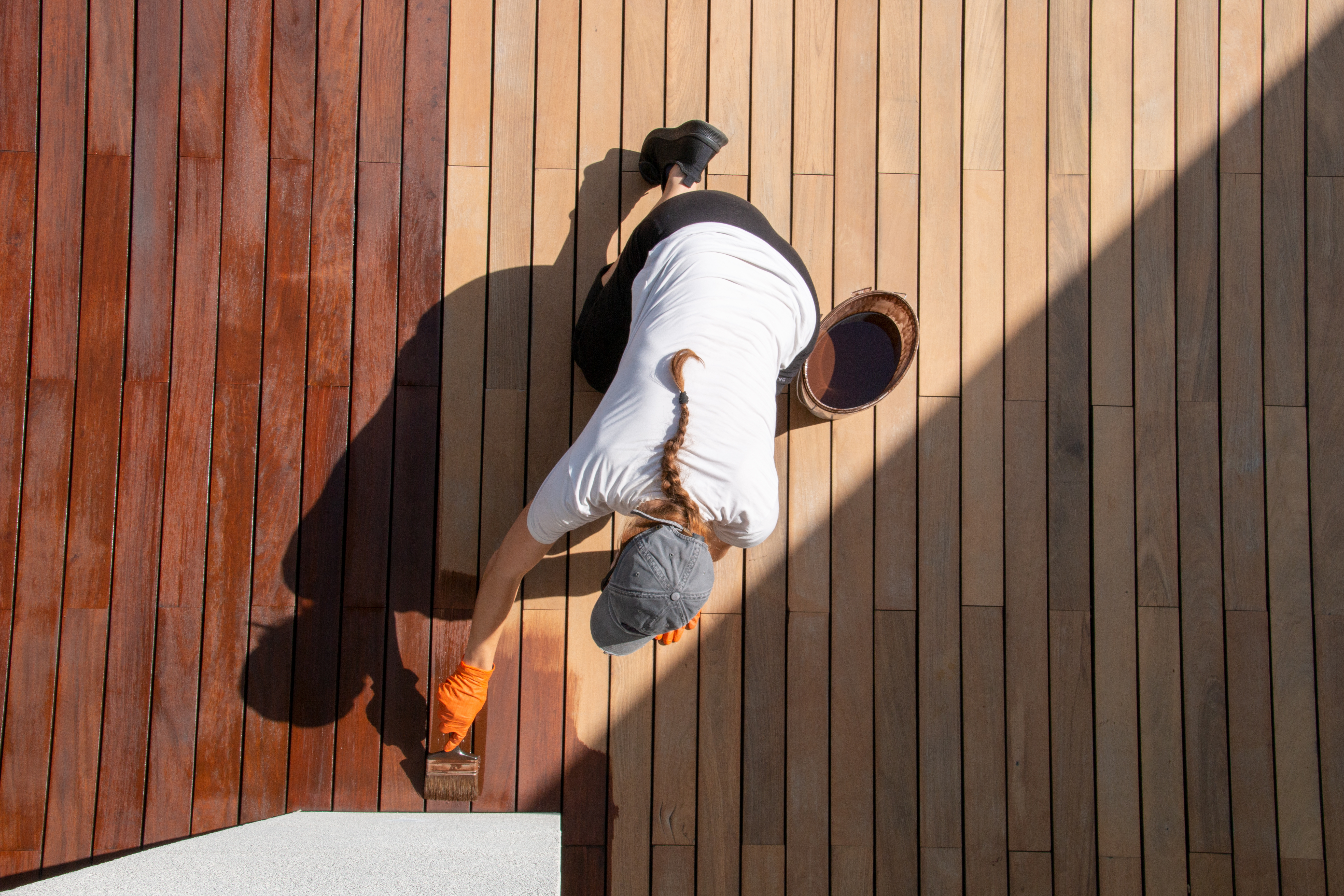 Coating with protective outdoor UV wood finish on the wooden surface of the lining boards, female worker with paintbrush overhead view